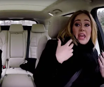 A person sitting in a car expressing excitement, gesturing with hands, and looking towards the right.