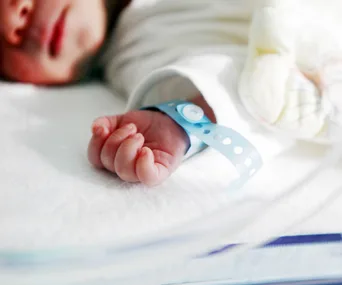 Newborn baby lying on a hospital bed with a blue identification wristband.
