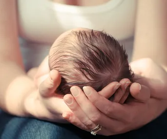 A tender moment capturing a baby’s head cradled gently in an adult's hands.