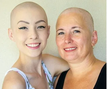 Mother and daughter with shaved heads smiling, supporting each other in breast cancer battle.