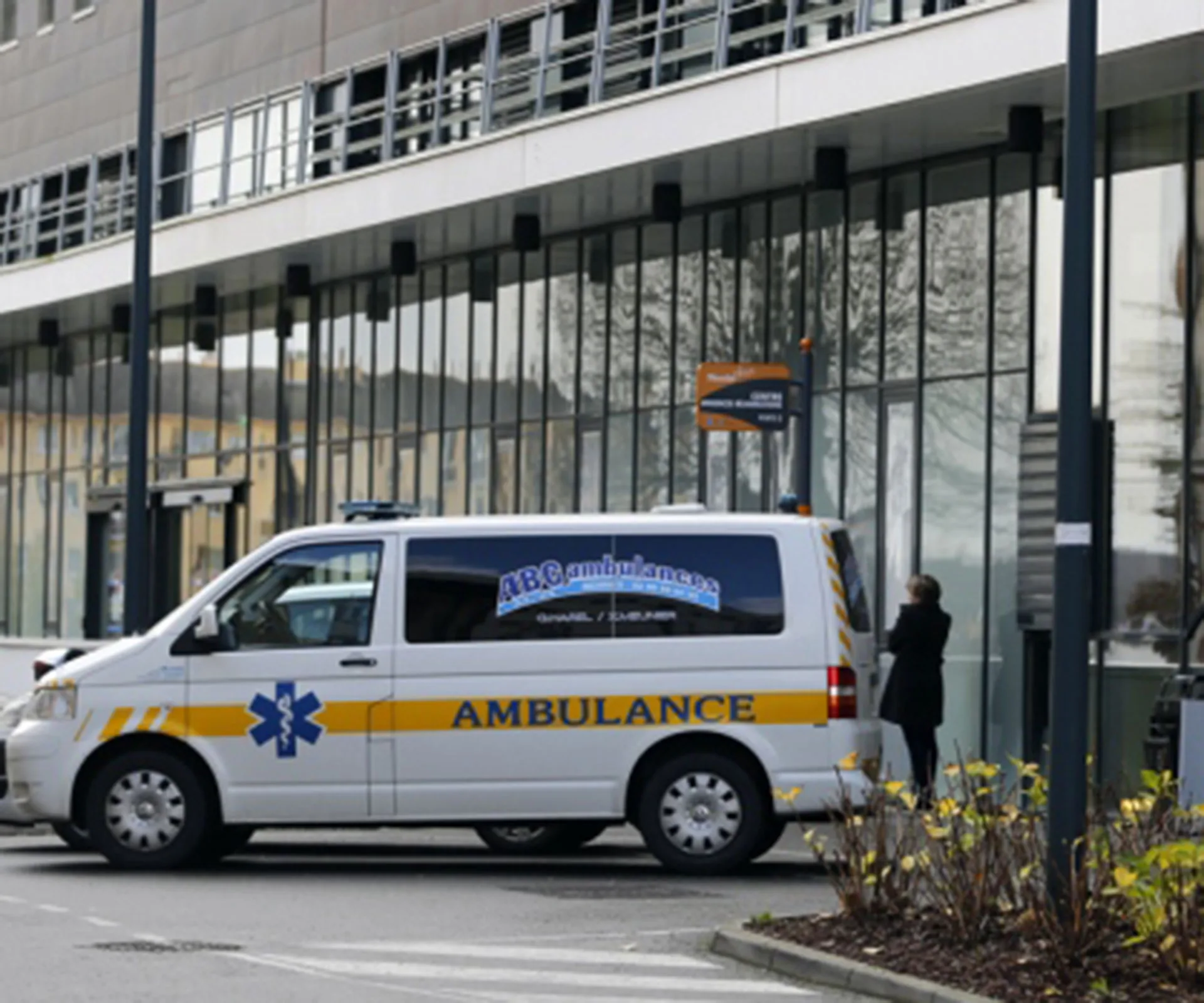 Ambulance parked outside a modern hospital building with a person standing nearby.