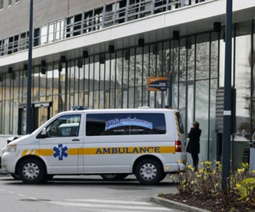 Ambulance parked outside a modern hospital building with a person standing nearby.