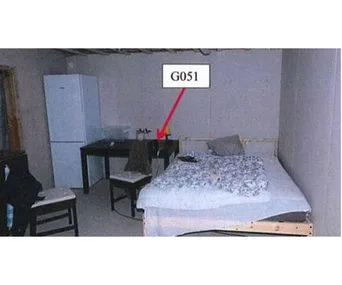 Room with a bed, table, chair, and fridge. Red arrow pointing at item on table labeled "G051".