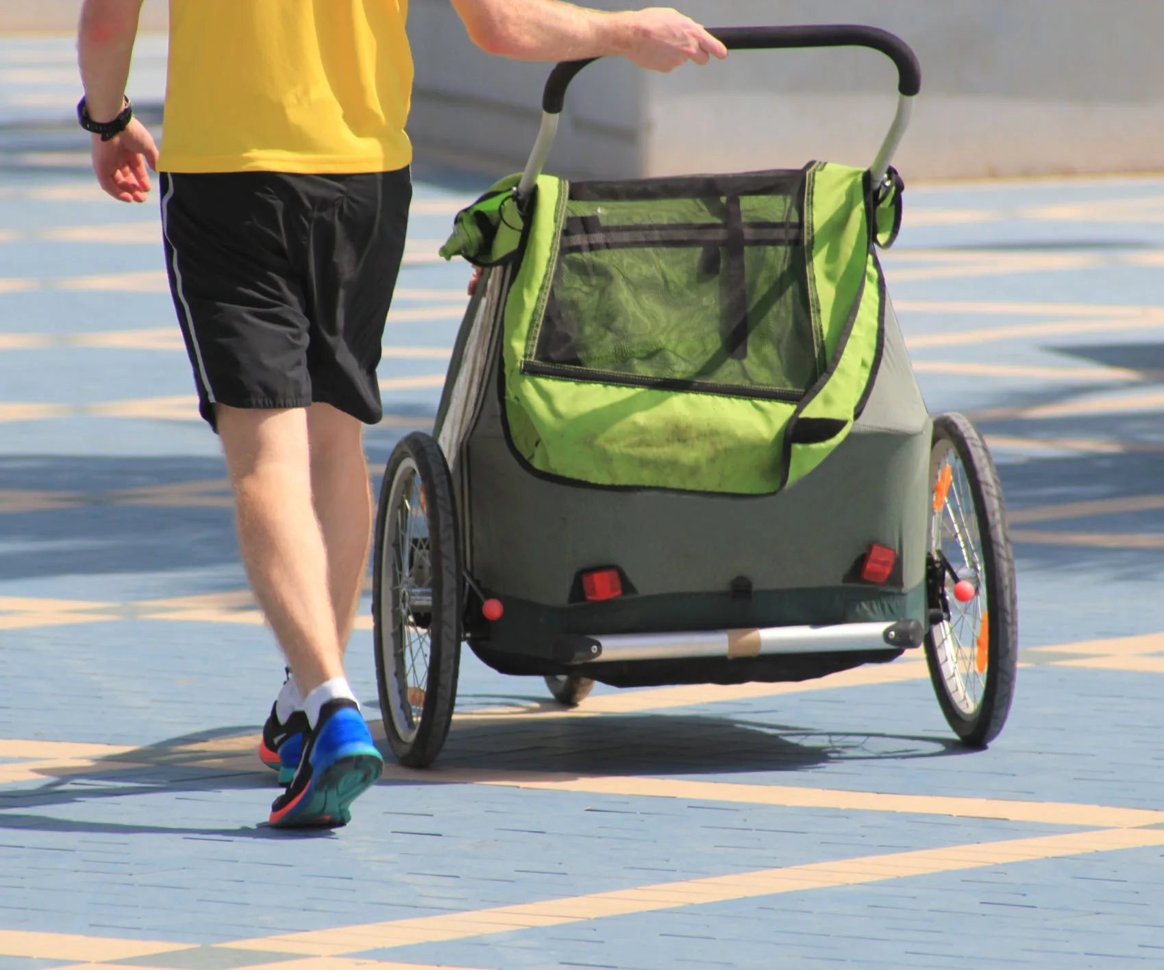 Man in yellow shirt pushing a green stroller on a blue tiled path.