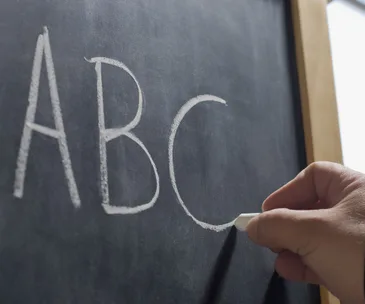 Hand writing "ABC" on a chalkboard with white chalk.