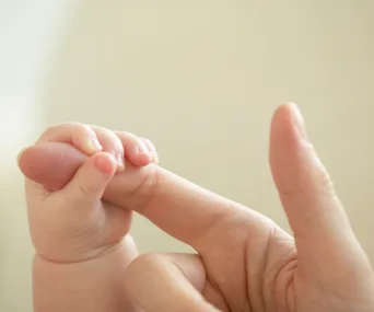 "Close-up of a baby holding an adult's finger, soft focus background."