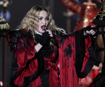 A performer in a red and black outfit sings passionately on stage, holding a microphone.