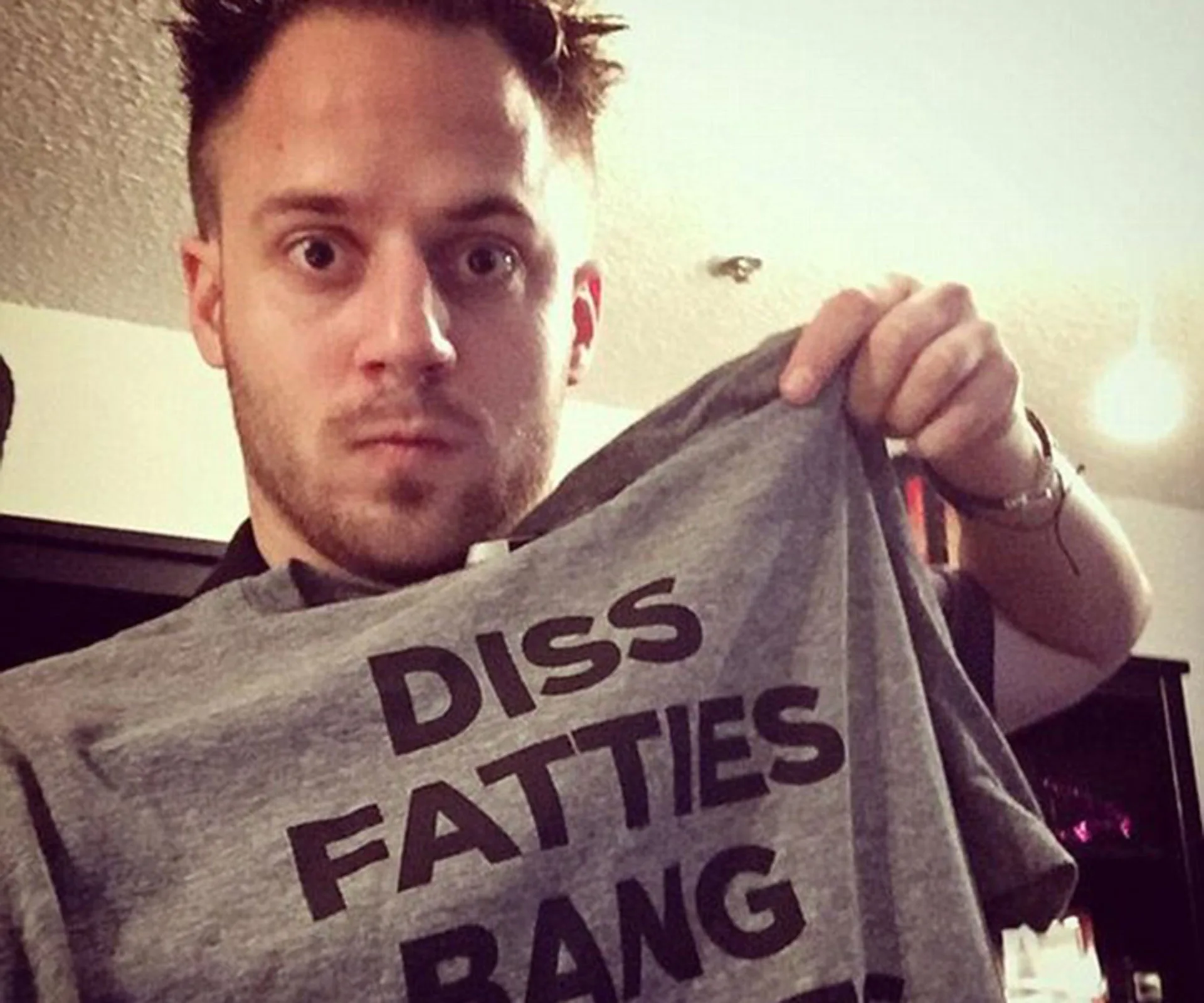 Man holding a gray T-shirt with offensive black text.
