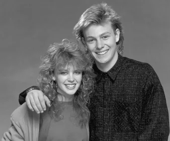 A black and white photo of a smiling young man and woman, standing closely together, hugging.