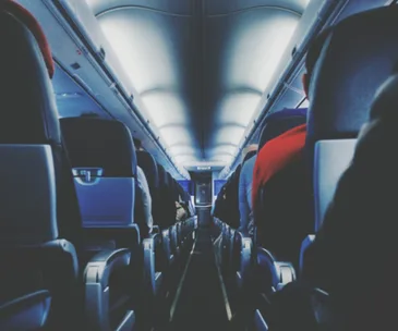 Interior view of an airplane cabin with rows of seats on either side and passengers seated.