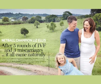 Family standing happily in a grassy field, smiling; woman in a white dress, man in a blue shirt, and a young girl in blue.