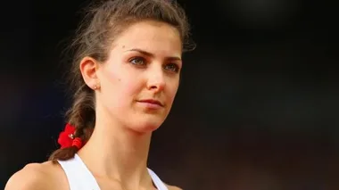 Young female athlete with braided hair and a red ribbon, wearing a white tank top, looking focused.