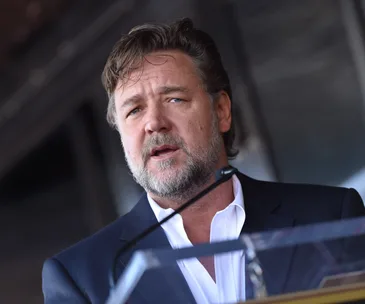 Adult man in a suit speaking at a podium, background blurred.