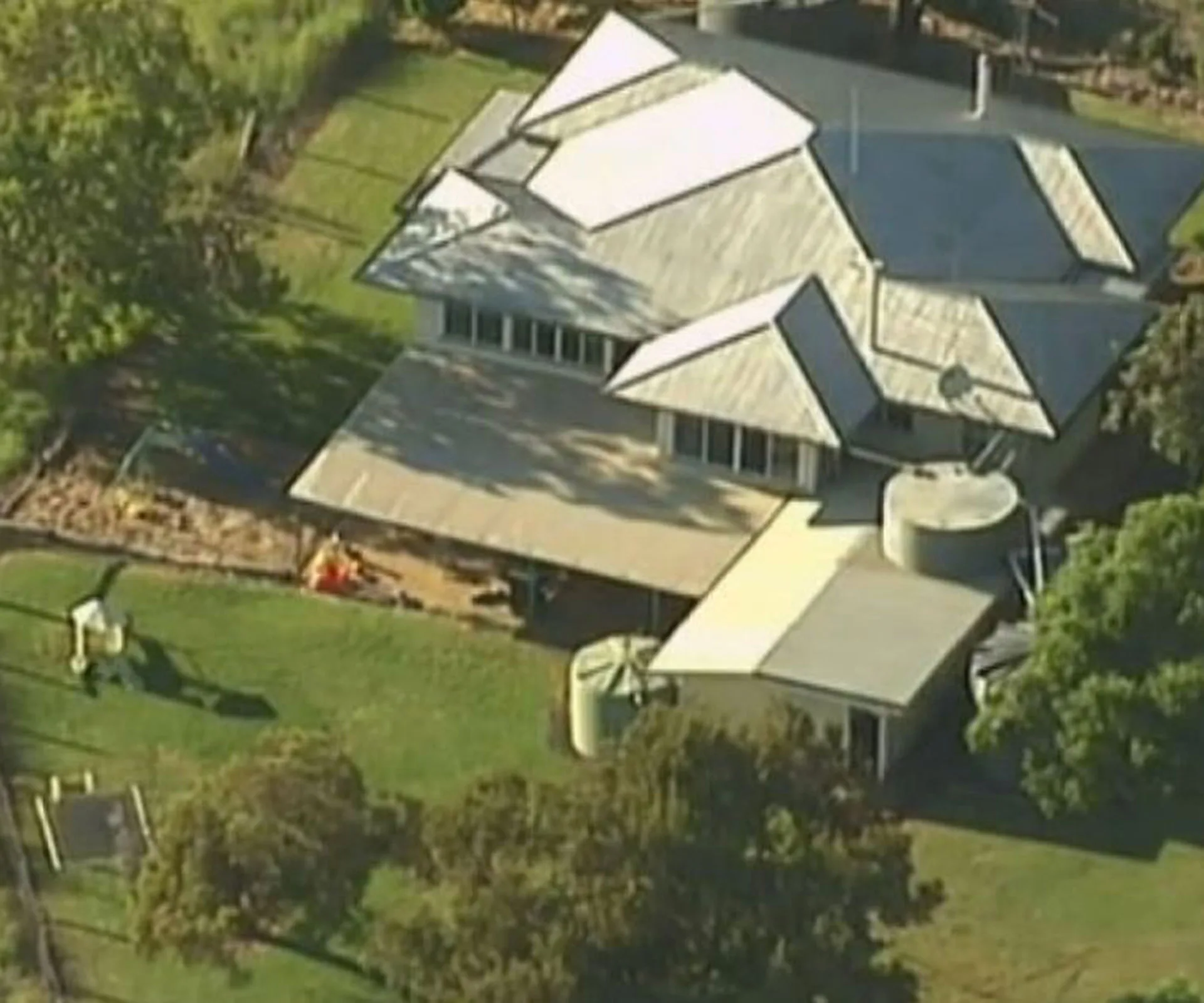 Aerial view of a house with a metal roof, surrounded by trees and a grassy yard.