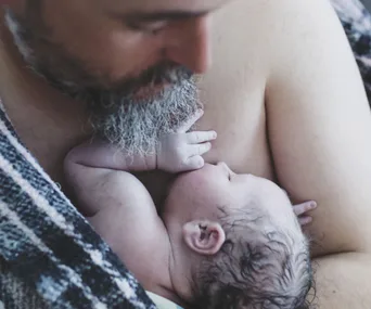 Father lovingly cradles newborn baby against his chest, wrapped in a blanket for warmth.
