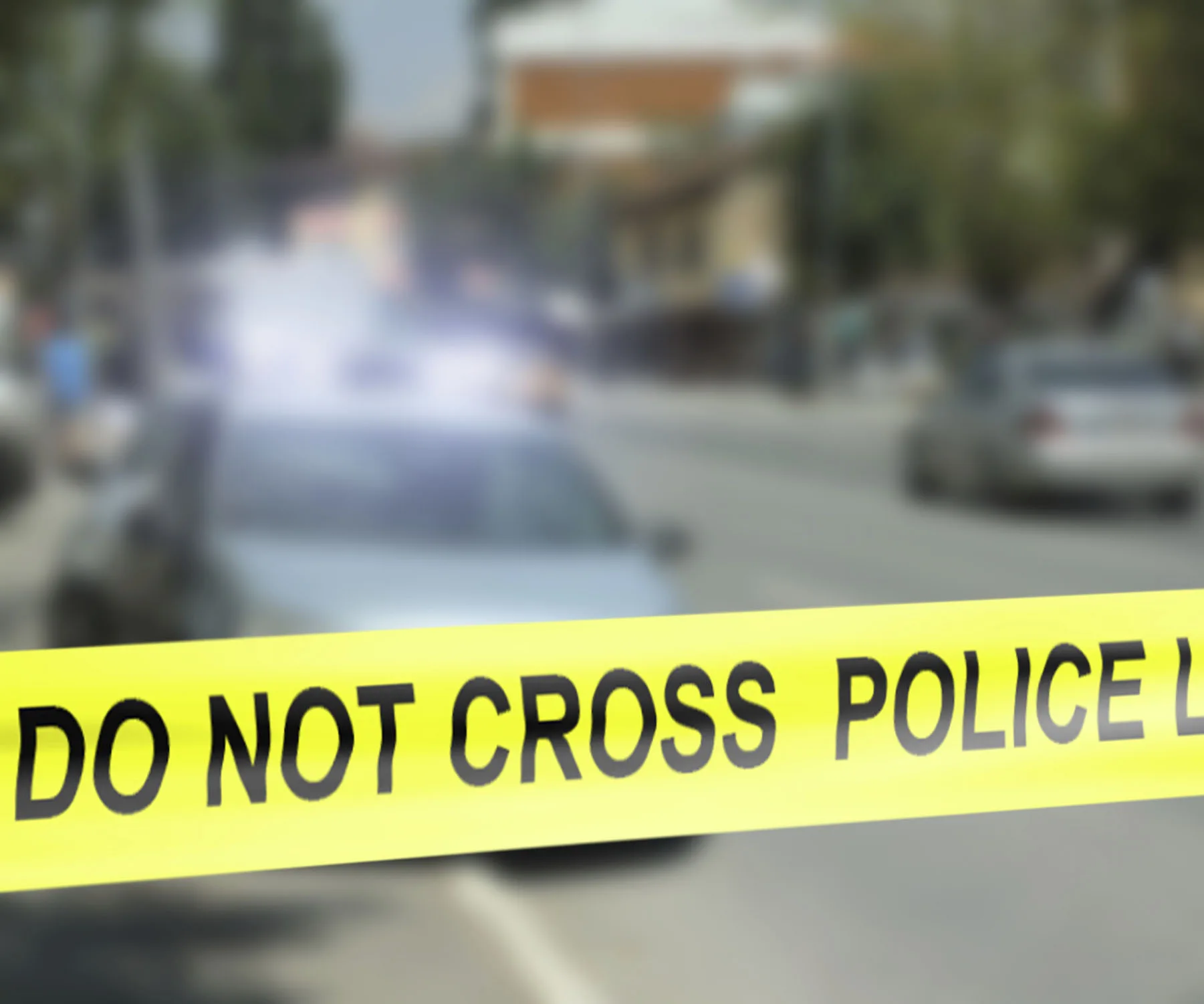 Blurred street scene with a police car and yellow "Do Not Cross Police Line" tape in the foreground.