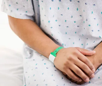 A person in a hospital gown with hands resting on their lap wearing a green wristband.