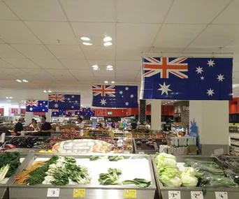 Supermarket interior with flipped Australian flags hanging from the ceiling above fresh produce displays.