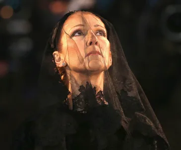 A woman in mourning attire, looking upwards, with a veil covering her face.