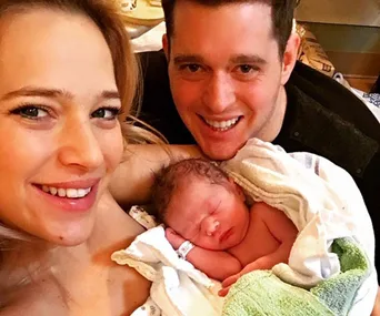 Smiling couple holding their newborn baby, wrapped in a blanket.