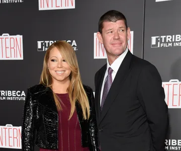 A man in a black suit and a woman in a black jacket smile at a film premiere event backdrop.