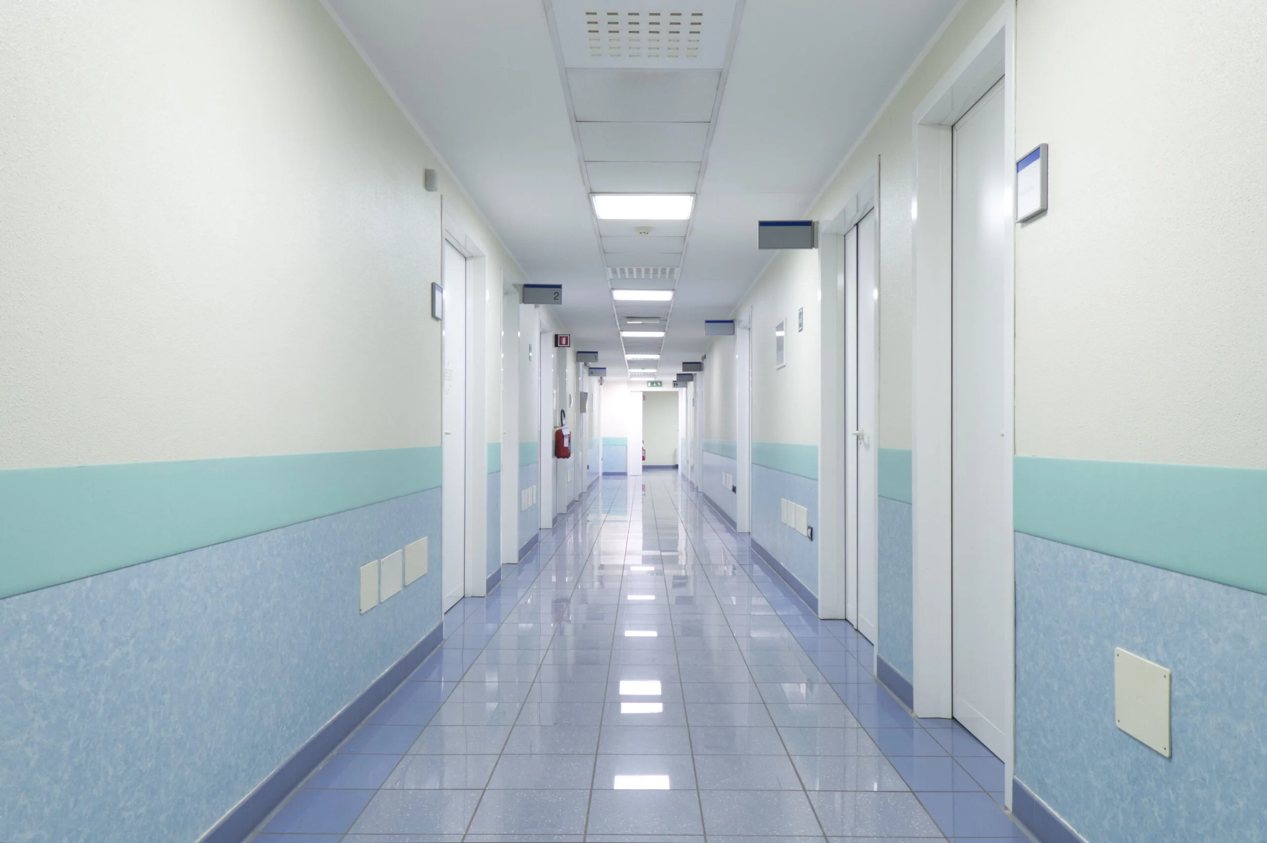A clean hospital corridor with closed doors and fluorescent lighting.