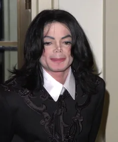 A person in a costume resembling Michael Jackson, wearing a black suit with embroidery and a white collar.