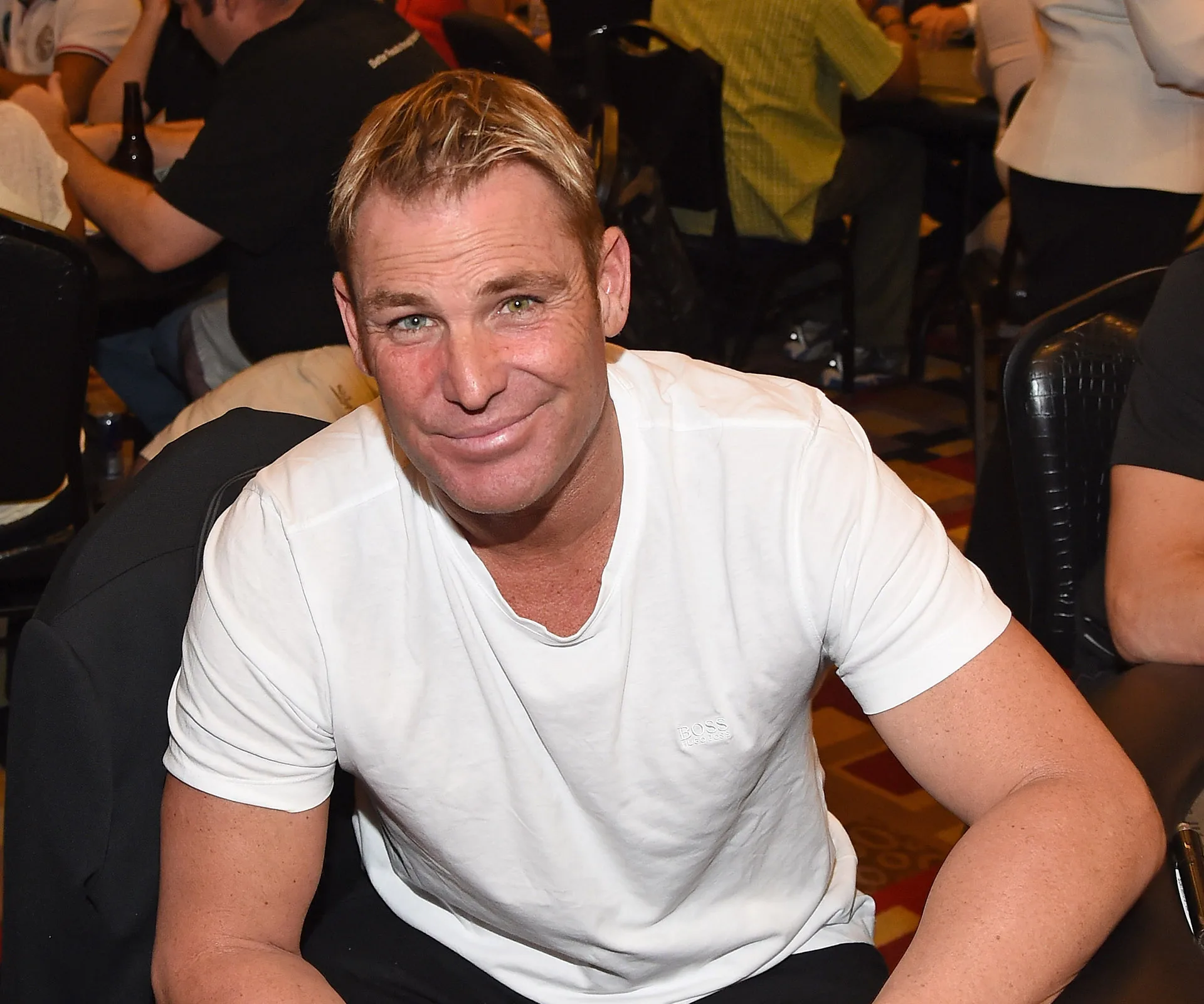 A person in a white t-shirt smiling at a table with others in the background.