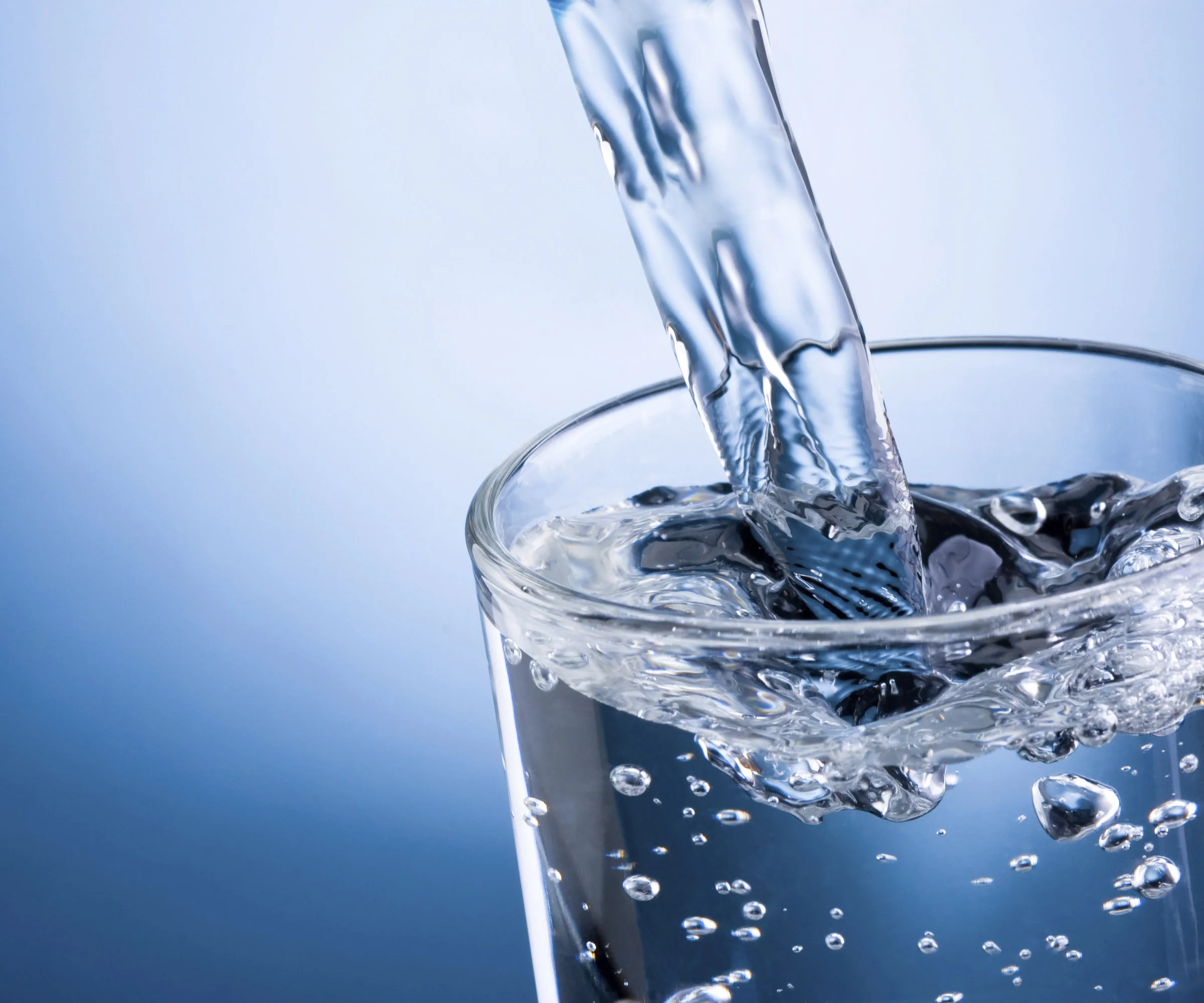 Pouring water into a clear glass against a blue background, with bubbles forming.