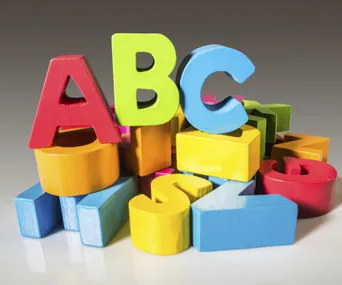 Colorful wooden alphabet blocks arranged in a pile with A, B, C on top.