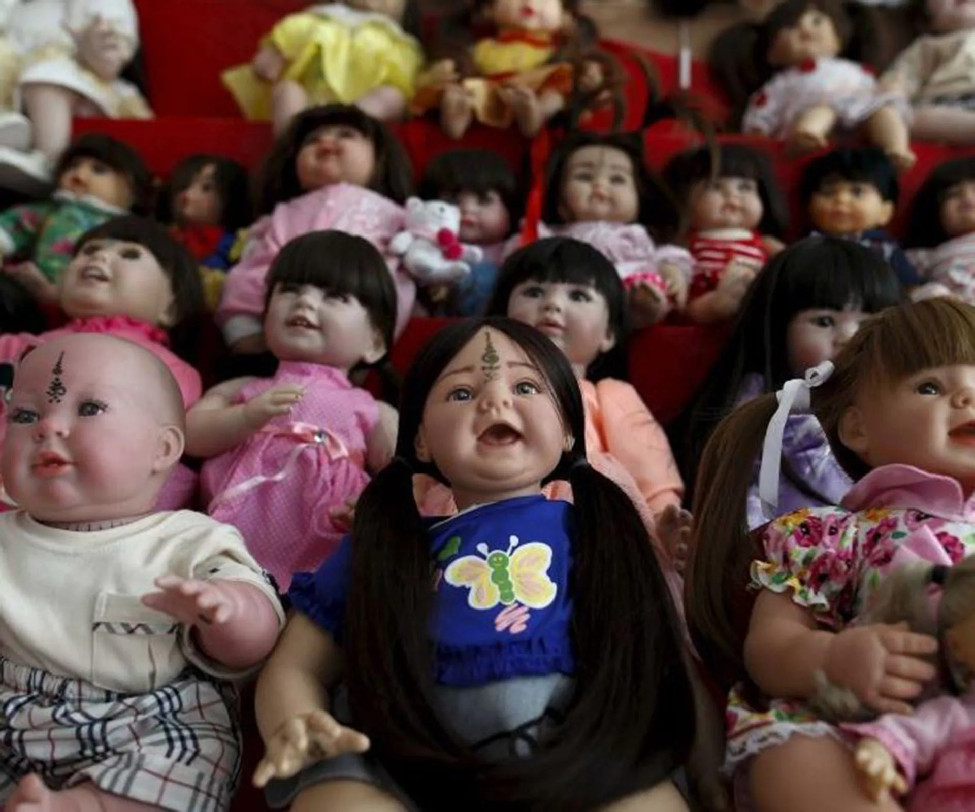 Several lifelike dolls with varied expressions and hairstyles are seated closely together.