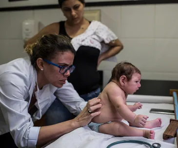 Doctor examines a baby as a concerned woman observes in a clinical setting.