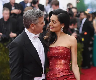Couple smiling at each other on red carpet, surrounded by photographers.