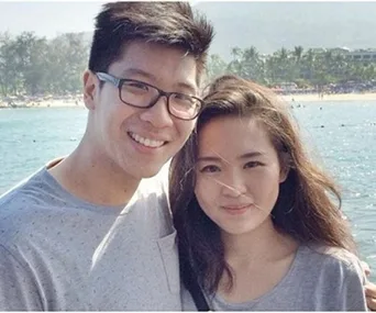A smiling man and woman posing outdoors with a beach and ocean backdrop.