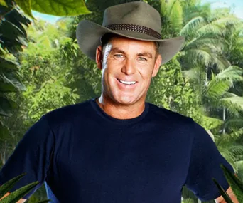 A man in a blue shirt and hat stands smiling in a jungle setting.