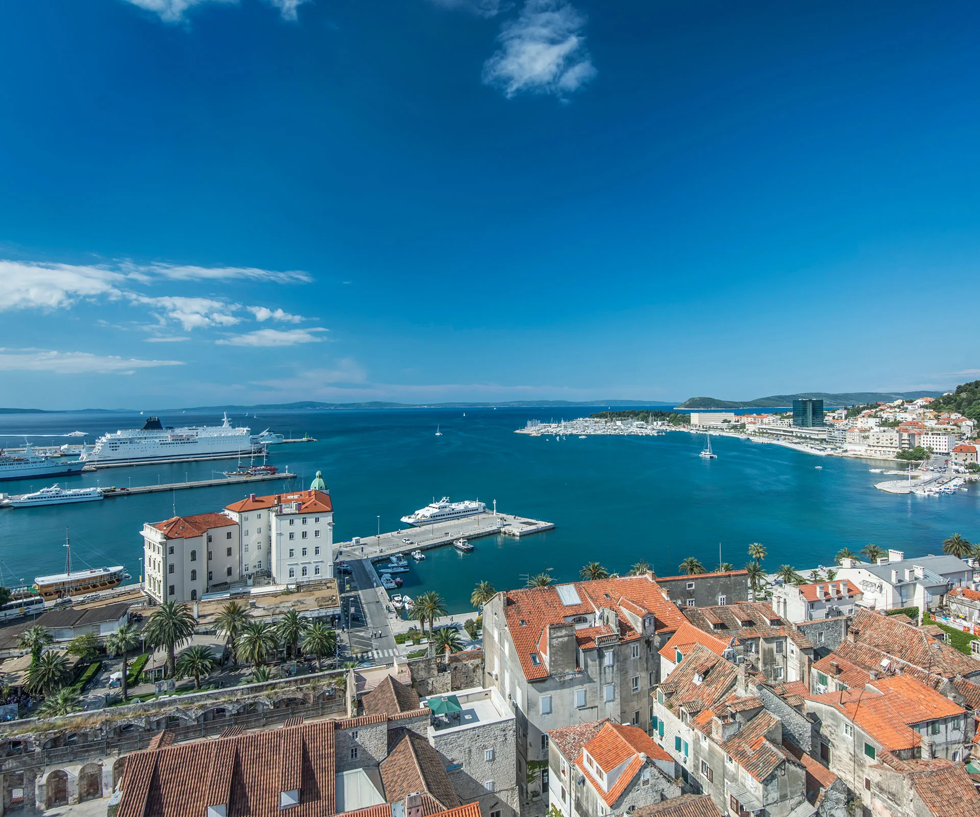 Coastal cityscape with harbor, cruise ships, and historic buildings under a clear blue sky.