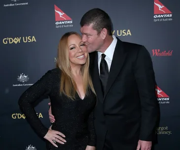 Two people posing on a red carpet; one is kissing the other's cheek while she smiles widely, wearing a sparkling dress.
