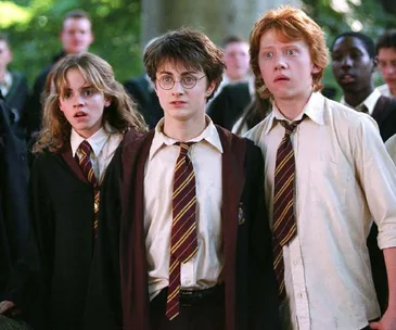 Hermione, Harry, and Ron look surprised in their Hogwarts uniforms in a scene from the Harry Potter series.
