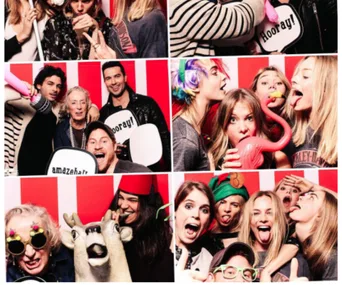 Group of people having fun in a photo booth, some wearing costumes, holding props, and making funny faces.