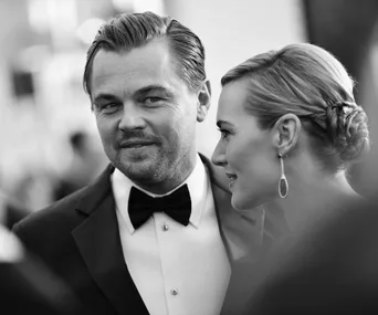 Black and white photo of a man in a tuxedo and a woman in an elegant hairstyle, appearing to smile at an event.