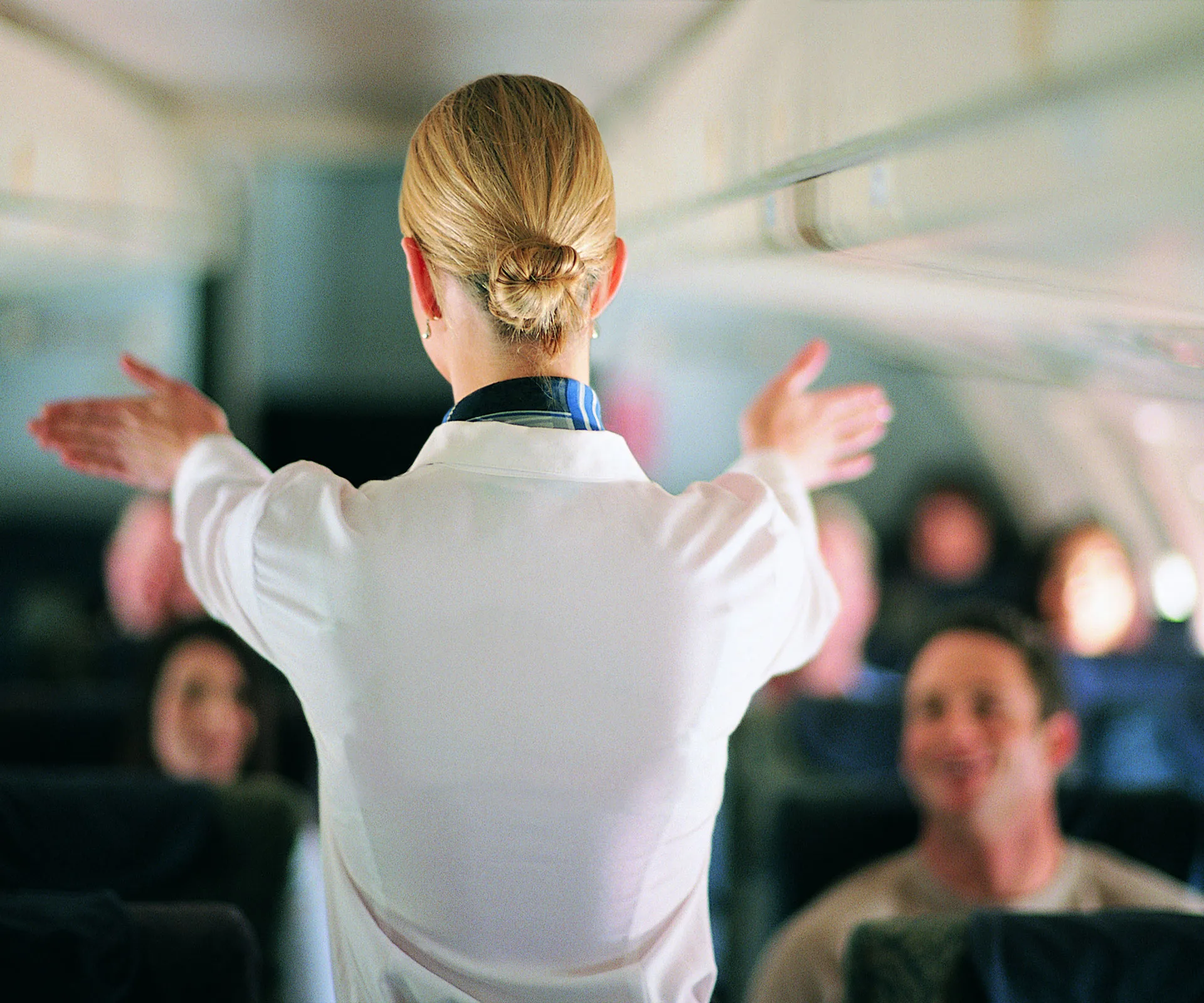 A flight attendant demonstrating safety procedures to passengers in an airplane cabin.