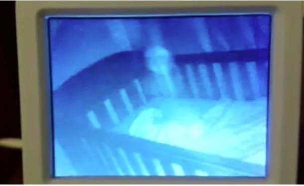 Baby monitor display showing a ghost-like figure near a sleeping child in a crib at night.