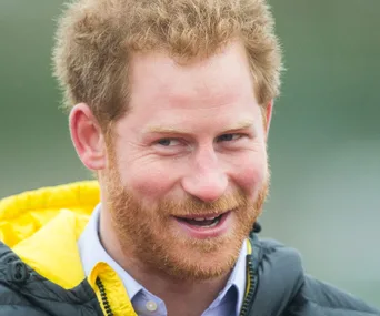 A person with reddish-brown hair and a beard, smiling, wearing a black and yellow jacket outdoors.