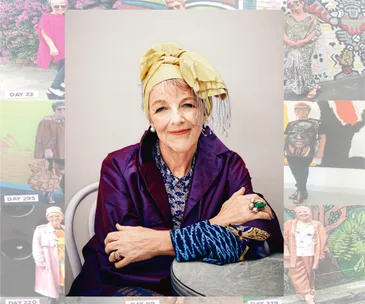 Elderly woman in a vibrant outfit, wearing a headscarf and jewelry, sitting with arms crossed on a gray chair.