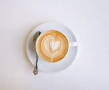 Cup of coffee with heart-shaped latte art on a saucer with a spoon.