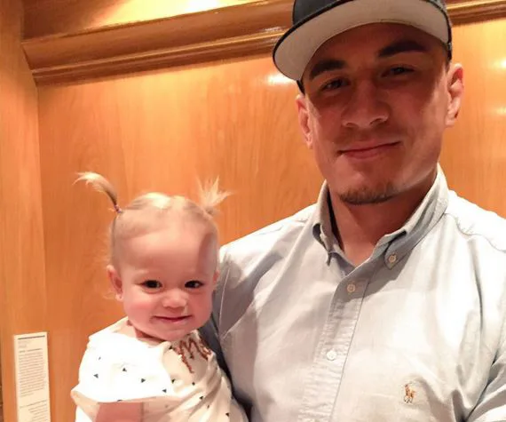 Father wearing a cap holding a smiling toddler with pigtails in an elevator.