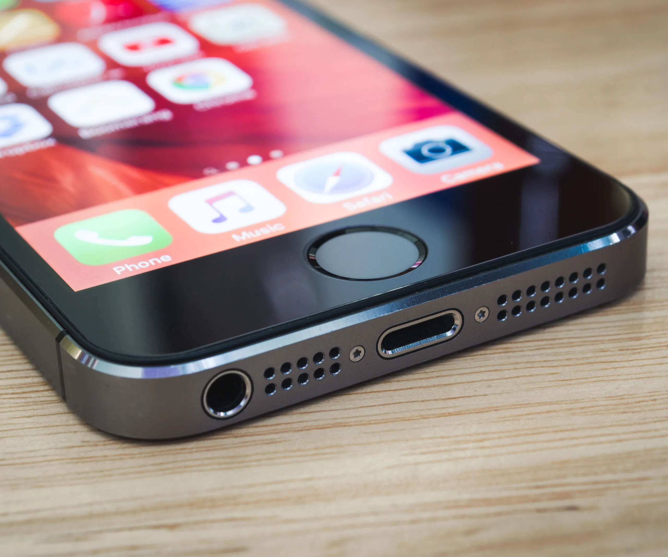 Close-up of an iPhone's bottom, showing the charging port and headphone jack on a wooden surface.