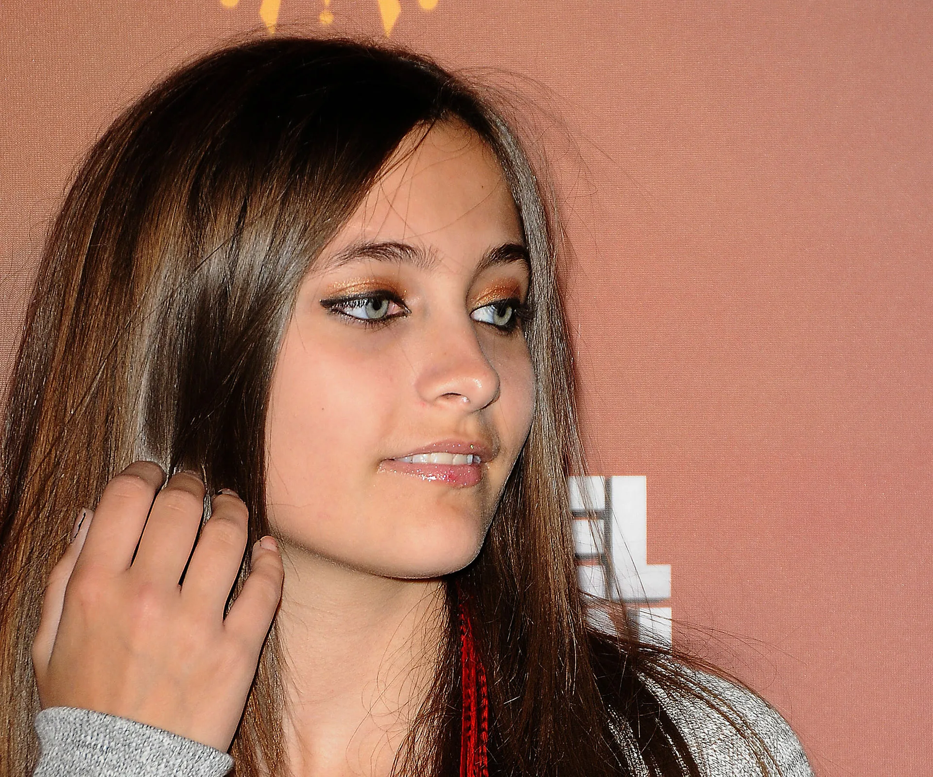 Young woman with long hair and makeup, looking off-camera, against a warm-toned background.