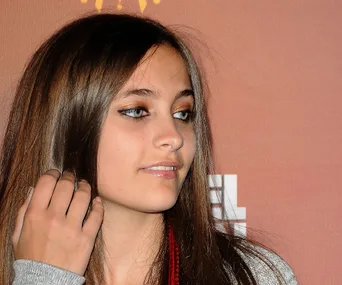 Young woman with long hair and makeup, looking off-camera, against a warm-toned background.