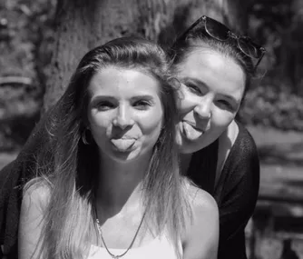 Two women outdoors sticking their tongues out playfully, black and white photo.